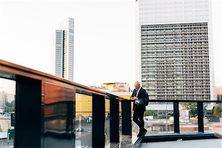 simsearch:649-09061360,k - Mature businessman standing outdoors, holding motorcycle helmet, using smartphone Photographie de stock - Premium Libres de Droits, Code: 649-09061349