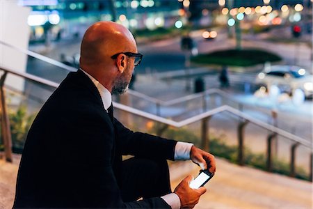 simsearch:649-09061360,k - Mature businessman outdoors at night, sitting on steps, holding smartphone Photographie de stock - Premium Libres de Droits, Code: 649-09061360