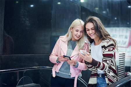 Two young women moving up underground station escalator  looking at smartphone Stock Photo - Premium Royalty-Free, Code: 649-09061455