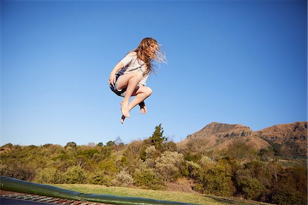 Young girl jumping on trampoline, mid air, in rural setting Stock Photo - Premium Royalty-Free, Code: 649-09061478