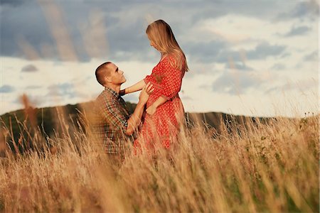 Mid adult man kneeling with hand on pregnant wife's stomach in field Foto de stock - Royalty Free Premium, Número: 649-09061912