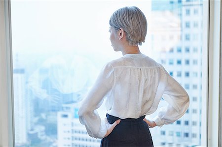 simsearch:6116-07085230,k - Rear view of businesswoman, hands on hips, looking out of window Stock Photo - Premium Royalty-Free, Code: 649-09061973