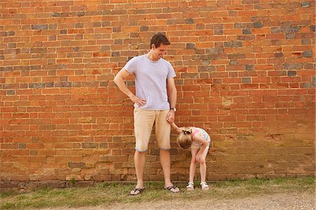 Girl bending forward holding father's hand by brick wall Stock Photo - Premium Royalty-Free, Code: 649-09077949