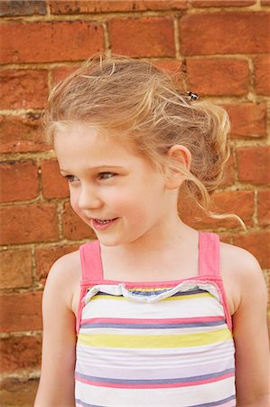 elementary age - Girl with blond pony tail looking away by brick wall Stock Photo - Premium Royalty-Free, Code: 649-09077954