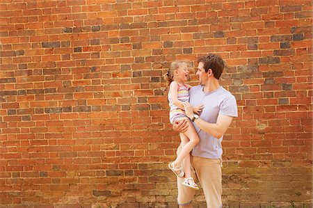 Girl laughing in father's arms by brick wall Stock Photo - Premium Royalty-Free, Code: 649-09077950