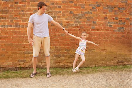 Girl leaning sideways holding father's hand by brick wall Stock Photo - Premium Royalty-Free, Code: 649-09077951