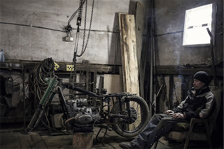 Mechanic sitting in armchair smoking cigarette in workshop with dismantled vintage motorcycle Stock Photo - Premium Royalty-Free, Code: 649-09077965