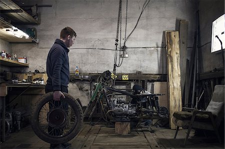 Mechanic carrying vintage motorcycle wheel in workshop Stock Photo - Premium Royalty-Free, Code: 649-09077969