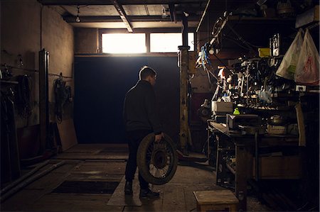 retro repair - Mechanic carrying vintage motorcycle wheel in workshop Stock Photo - Premium Royalty-Free, Code: 649-09077971