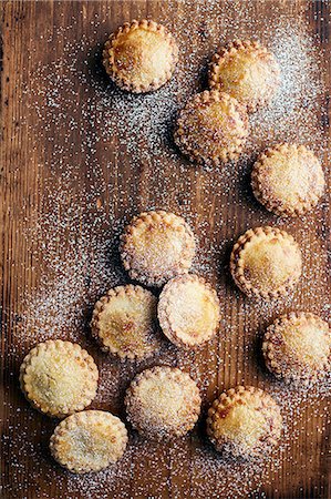 Freshly baked mince pies, dusted with sugar, on wooden counter, overhead view Stock Photo - Premium Royalty-Free, Code: 649-09078026