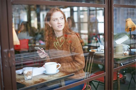 simsearch:614-06813943,k - View through window of woman at coffee shop using mobile phone Photographie de stock - Premium Libres de Droits, Code: 649-09078072