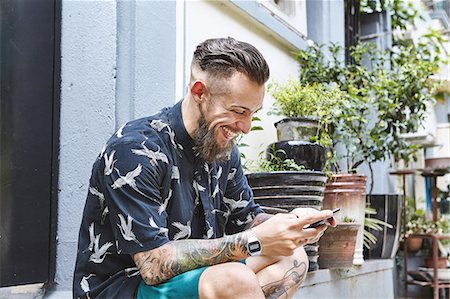 Young man sitting on doorstep in residential alleyway looking at smartphone, Shanghai French Concession, Shanghai, China Stock Photo - Premium Royalty-Free, Code: 649-09078391