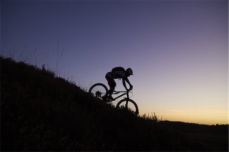 Silhouetted male mountain biker biking down hill at sunset Stock Photo - Premium Royalty-Free, Code: 649-09078454