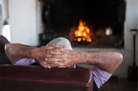 Rear view of senior man at home with hands behind his head in front of log fire Photographie de stock - Premium Libres de Droits, Code: 649-09078662