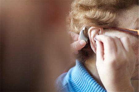 simsearch:614-08884947,k - Mature woman helping senior woman insert hearing aid, close-up, differential focus Foto de stock - Royalty Free Premium, Número: 649-09111582