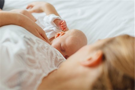 sein allaitant - Young woman lying on bed with baby daughter, cropped Photographie de stock - Premium Libres de Droits, Code: 649-09111609