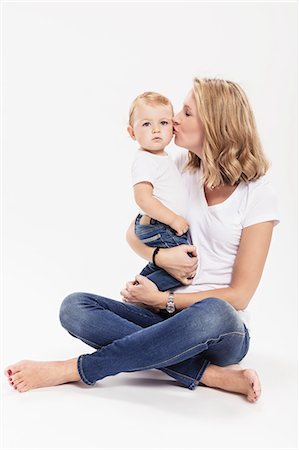 Studio portrait of woman sitting cross legged on floor kissing baby son Stock Photo - Premium Royalty-Free, Code: 649-09111645