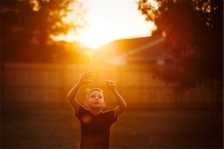 simsearch:649-06844269,k - Boy practicing american football in garden reaching for a catch at sunset Fotografie stock - Premium Royalty-Free, Codice: 649-09111692