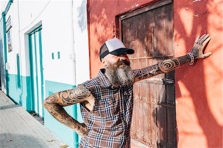 simsearch:649-09123411,k - Tattooed male hipster leaning against sunlit wall Stock Photo - Premium Royalty-Free, Code: 649-09123406