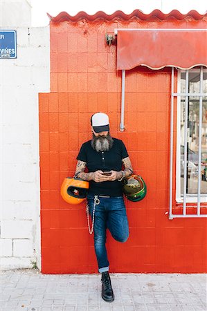 simsearch:649-09078395,k - Male hipster leaning against red wall looking at smartphone Fotografie stock - Premium Royalty-Free, Codice: 649-09123402