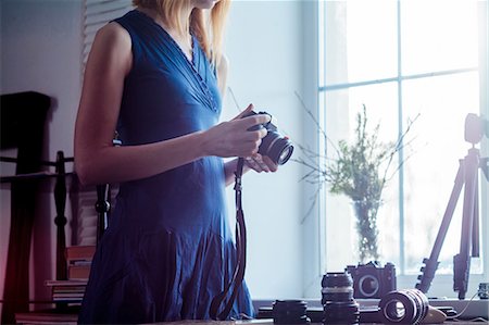 Mid adult woman, beside window, holding camera, camera lenses on table in front of her, mid section Stock Photo - Premium Royalty-Free, Code: 649-09123535