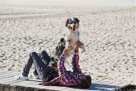 simsearch:649-08840788,k - Man lying on beach boardwalk playing with dog Foto de stock - Sin royalties Premium, Código: 649-09123630