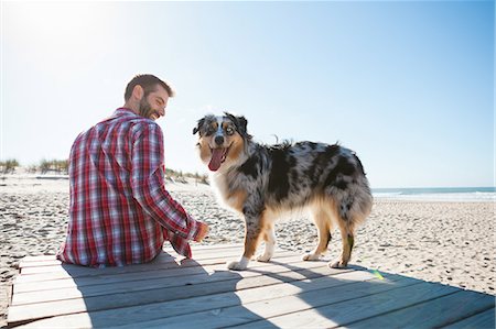 dog looking over shoulder - Man sitting on beach boardwalk with dog Stock Photo - Premium Royalty-Free, Code: 649-09123631