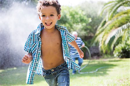 play with water on garden - Boy running away from grandfather spraying hosepipe in garden Stock Photo - Premium Royalty-Free, Code: 649-09123645