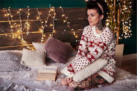 portrait tattoos of women - Young woman sitting on bed, wearing christmas jumper, thoughtful expression Stock Photo - Premium Royalty-Free, Code: 649-09123655