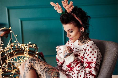 Young woman sitting at home, wearing christmas jumper and antlers, drinking hot drink Stock Photo - Premium Royalty-Free, Code: 649-09123651