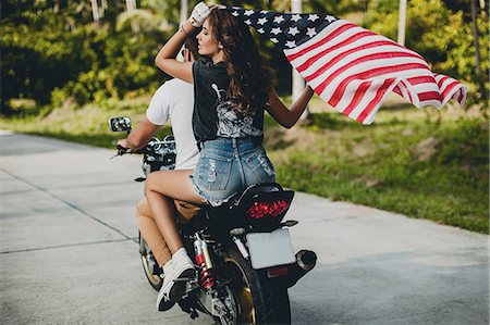 Young couple holding up American flag while riding motorcycle on rural road, Krabi, Thailand, rear view Stock Photo - Premium Royalty-Free, Code: 649-09123885