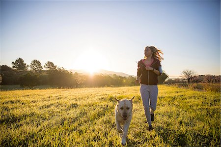 Young woman running across field, with pet dog Stock Photo - Premium Royalty-Free, Code: 649-09139030