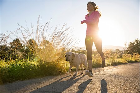 dog look up person - Young woman running along rural road with pet dog, low angle view Stock Photo - Premium Royalty-Free, Code: 649-09139032