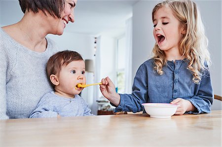 Family sitting at kitchen table, young girl spoon-feeding baby sister Photographie de stock - Premium Libres de Droits, Code: 649-09139246