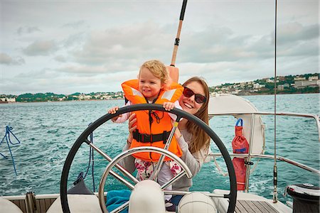 sailing yacht steering wheel - Woman steering yacht with toddler daughter, portrait, Devon, UK Stock Photo - Premium Royalty-Free, Code: 649-09148603