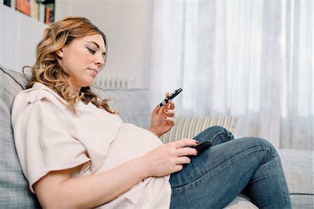 simsearch:649-08577535,k - Pregnant woman on sofa looking at blood sugar test result Stock Photo - Premium Royalty-Free, Code: 649-09148625