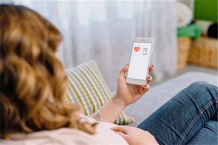 simsearch:614-08726746,k - Pregnant woman on sofa looking at heart rate on smartphone, over shoulder view Foto de stock - Royalty Free Premium, Número: 649-09148623