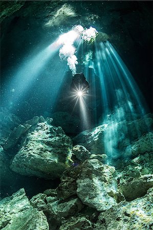 Male diver diving in underground river (cenote) with sun rays and rock formations, Tulum, Quintana Roo, Mexico Stock Photo - Premium Royalty-Free, Code: 649-09148843