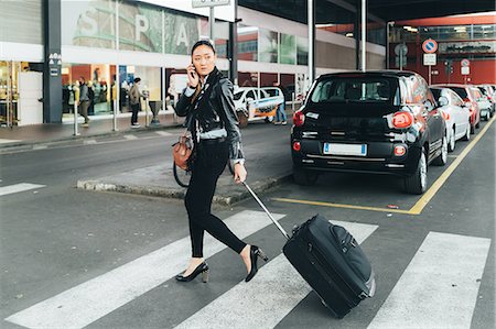 simsearch:614-08030826,k - Woman walking outdoors, pulling wheeled suitcase, talking on smartphone Stock Photo - Premium Royalty-Free, Code: 649-09148892