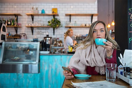 simsearch:649-09078072,k - Woman sitting in cafe, holding smartphone, drinking coffee Photographie de stock - Premium Libres de Droits, Code: 649-09149128