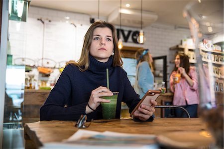 excluido - Young woman sitting in cafe, holding smartphone, drinking smoothie Foto de stock - Sin royalties Premium, Código: 649-09156221