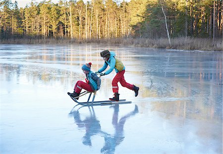 Boy pushing his brother on sleigh across frozen lake Stock Photo - Premium Royalty-Free, Code: 649-09166458
