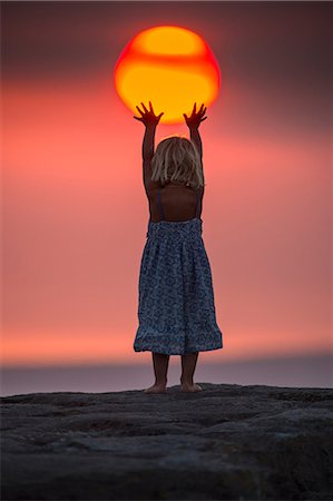 Young girl reaching up to touch setting sun, rear view, false perspective, Doolin, Clare, Ireland Stock Photo - Premium Royalty-Free, Code: 649-09167013