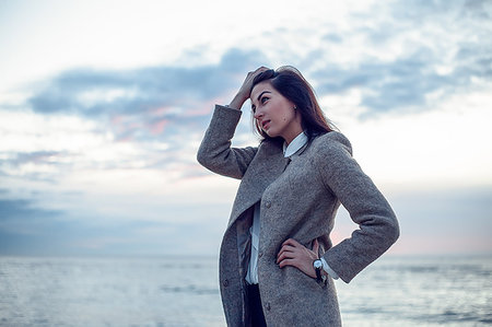 simsearch:614-08488009,k - Young woman standing on beach, hand keeping hair from face, thoughtful expression Stock Photo - Premium Royalty-Free, Code: 649-09176615