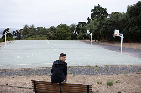 Male teenage basketball player looking back from park bench by basketball court Stock Photo - Premium Royalty-Free, Code: 649-09182144