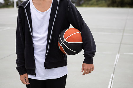 Male teenage basketball player on basketball court with ball under his arm, mid section Stock Photo - Premium Royalty-Free, Code: 649-09182153