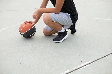 simsearch:649-09182176,k - Male teenage basketball player crouching with ball on basketball court, neck down Fotografie stock - Premium Royalty-Free, Codice: 649-09182167