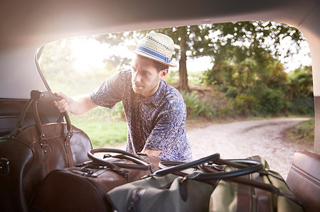 people packing luggage - Young man in trilby removing luggage from car boot on rural road Stock Photo - Premium Royalty-Free, Code: 649-09182437