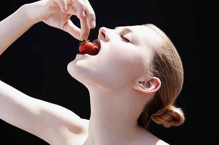 simsearch:649-09207472,k - Studio shot of young woman putting strawberry into her mouth Fotografie stock - Premium Royalty-Free, Codice: 649-09207462