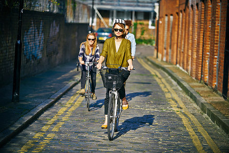 simsearch:6102-07843140,k - Front view of women wearing sunglasses  riding bicycles on cobblestone road Photographie de stock - Premium Libres de Droits, Code: 649-09209320